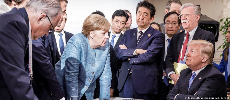 Angela Merkel (c., de pé) diante de Donald Trump na mesa de negociações do G7