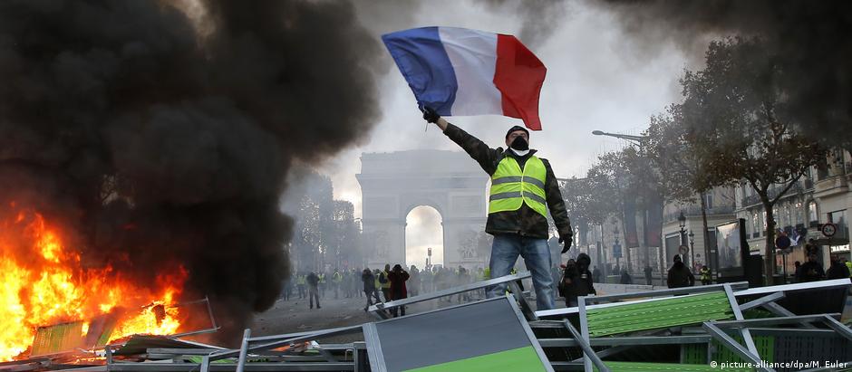 Manifestante dos "coletes amarelos" ergue a bandeira da França em barricada na avenida Champs-Élysées, em Paris